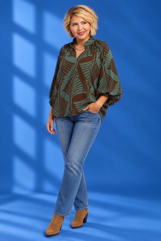A woman modeling a loose, long-sleeve blouse with a brown and green palm leaf pattern, paired with blue jean