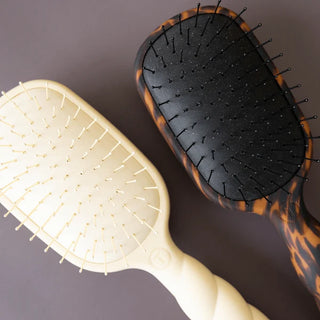 Two hairbrushes, one beige and one with tortoiseshell pattern, on a dark background.