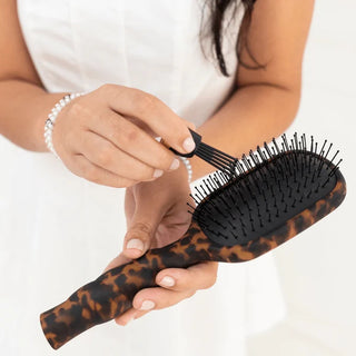 Person holding a tortoiseshell-patterned hairbrush with a white background