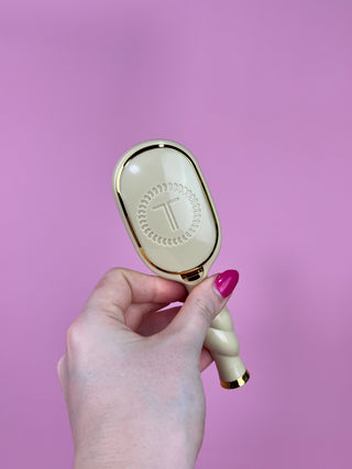 Hand holding a white and gold handheld mirror against a pink background