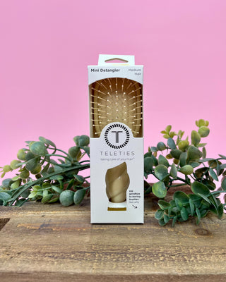 Teleties mini detangler packaging on a wooden surface with pink background and greenery