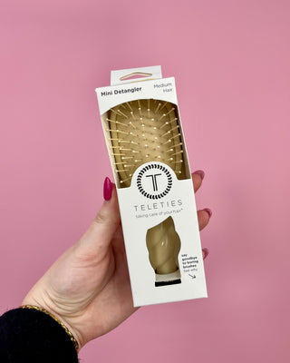 Hand holding a Teleties mini detangler packaging against a pink background