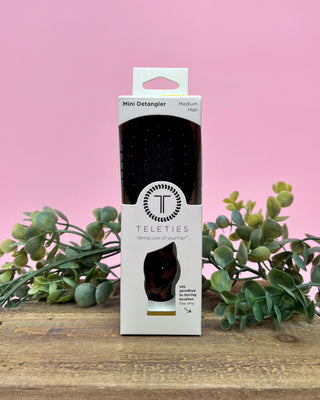Teleties mini detangler packaging on a wooden surface with pink background and greenery
