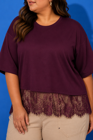 A woman wearing a short-sleeve crewneck top in deep burgundy with a matching lace hem, paired with beige pants