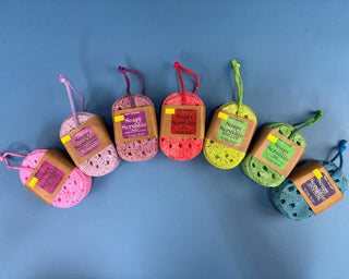 Six colorful handmade loofah soap sponges with hanging tags labeled 'Soap Scrub' arranged in a curved row