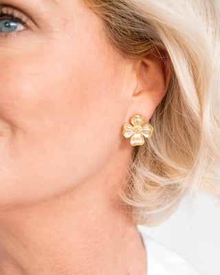 Close-up of a person wearing gold flower-shaped earrings.