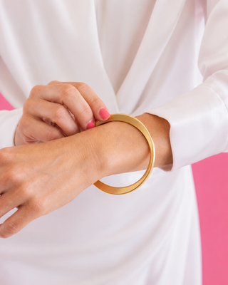 Gold bangle on a wrist with a white and pink background