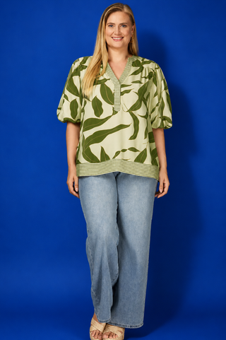 Woman wearing a green leaf-patterned top and blue jeans against a blue background