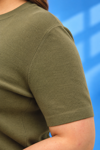Close-up of a person wearing an olive green short-sleeve knit top, showing the shoulder seam and ribbed fabric texture 