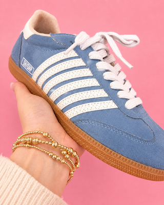 Blue sneaker with white stripes held by a hand against a pink background