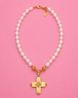 Pearl necklace with a gold cross pendant on a pink background