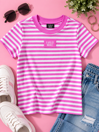A pink and white striped short-sleeve t-shirt with a pink chest patch reading 'LULU MAC' is styled in a flat lay on a pink background with white sneakers, blue jeans, sunglasses, and a small plant.