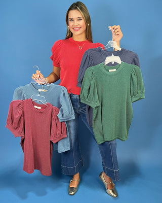 A woman modeling a red ribbed short-sleeve top with puff sleeves, paired with blue jeans