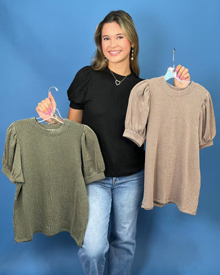 A woman modeling a red ribbed short-sleeve top with puff sleeves, paired with blue jeans