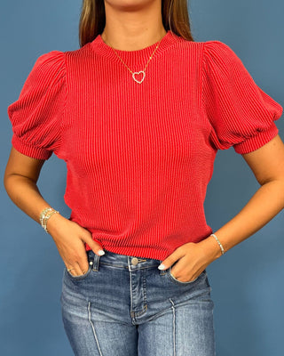 A woman modeling a red ribbed short-sleeve top with puff sleeves, paired with blue jeans
