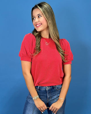 A woman modeling a red ribbed short-sleeve top with puff sleeves, paired with blue jeans