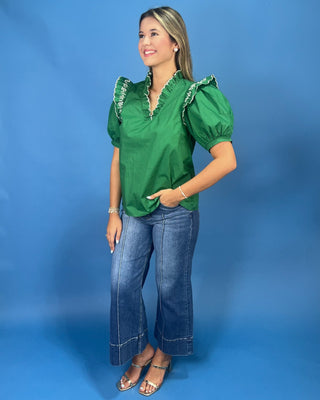 A woman modeling a vibrant green short-sleeve blouse with ruffled trim on the shoulders and neckline, paired with blue jeans