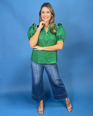 A woman modeling a bright green short-sleeve blouse with ruffled shoulders and a lace-up neckline, paired with wide-leg blu