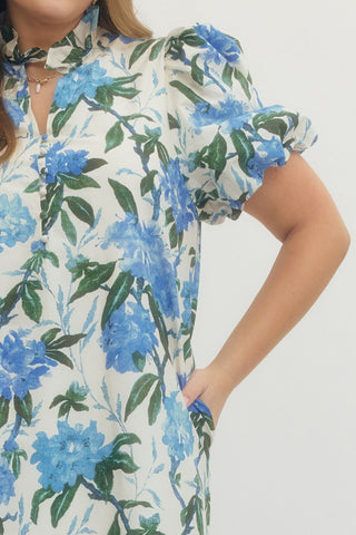 Woman wearing a floral dress with blue flowers and green leaves on a plain background