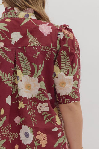Red floral dress with green leaves and white flowers on a plain background