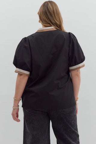 Person wearing a black blouse with beige trim on a plain background