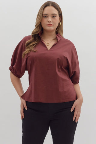 Woman wearing a burgundy blouse with short sleeves against a white background