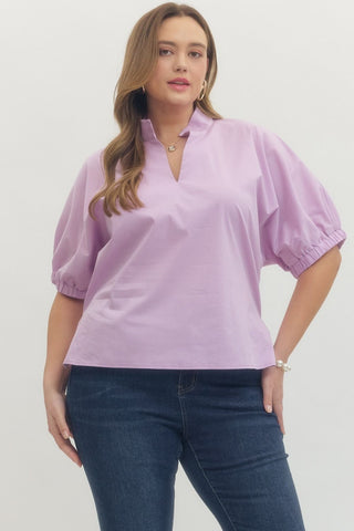 Woman wearing a light purple blouse with puffed sleeves and dark blue jeans on a white background