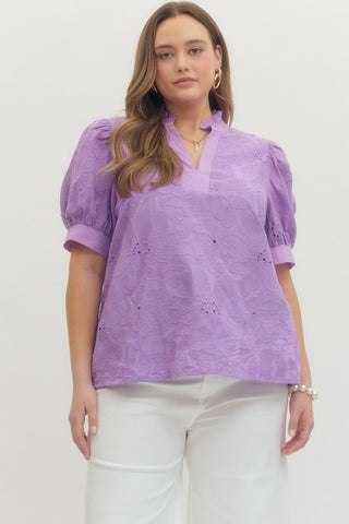 Woman wearing a purple blouse with white pants on a plain background
