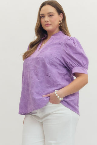 Woman wearing a purple blouse with white pants on a plain background