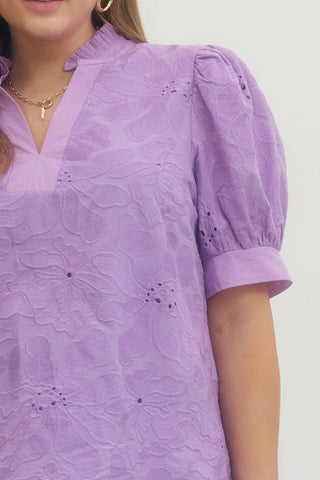 Close-up of a person wearing a purple patterned dress with puff sleeves on a plain background