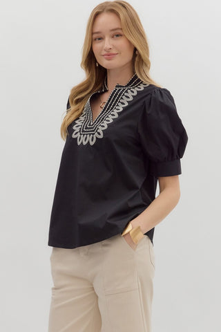 Woman wearing a black blouse with white embroidery on a plain background