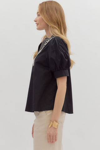 Woman wearing a black blouse with intricate detailing on a light gray background