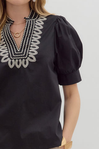 Black blouse with white embroidery on a plain background