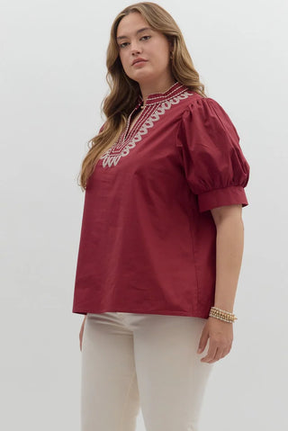 Woman wearing a burgundy blouse with white embroidery on a white background