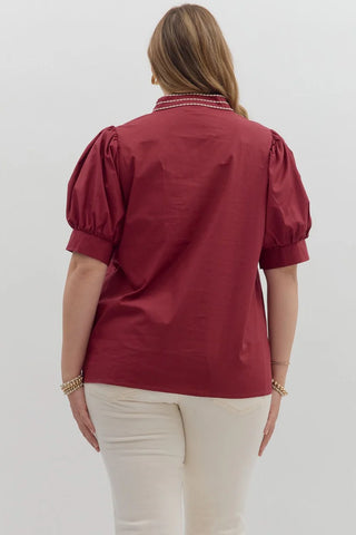 Woman wearing a burgundy blouse with short sleeves and a white background