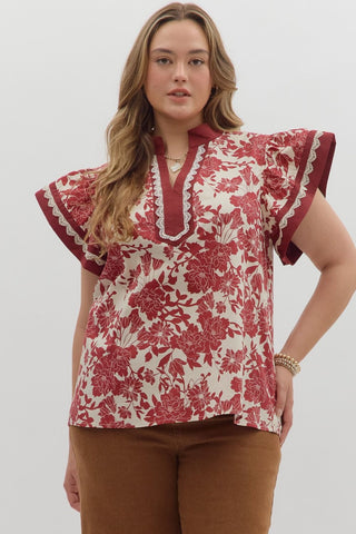 Woman wearing a red and white floral blouse with ruffled sleeves on a plain background