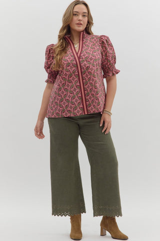 Woman wearing a pink patterned top and green pants on a white background