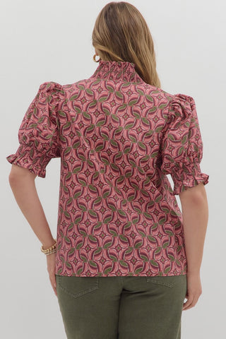 Woman wearing a pink patterned blouse with green pants on a white background