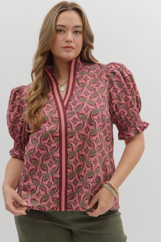 Woman wearing a pink patterned blouse with puff sleeves on a plain background