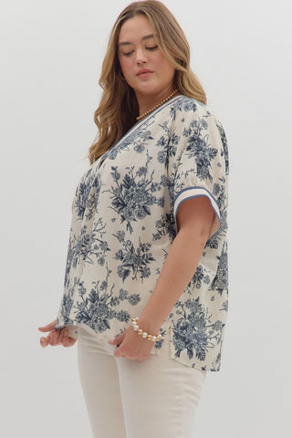 Woman wearing a floral blouse and white pants on a plain background