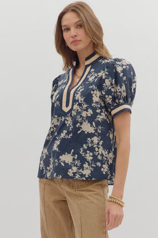Woman wearing a blue floral blouse with beige accents on a plain background