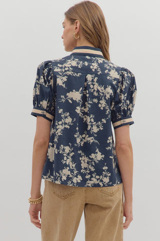 Person wearing a navy floral blouse with beige pants on a white background