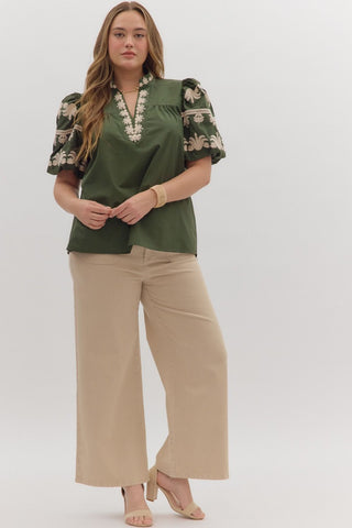 Woman wearing a green blouse with floral sleeves and beige pants on a white background