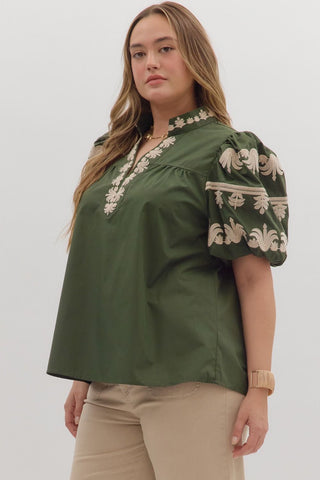 Woman wearing a green blouse with white embroidery on a plain background