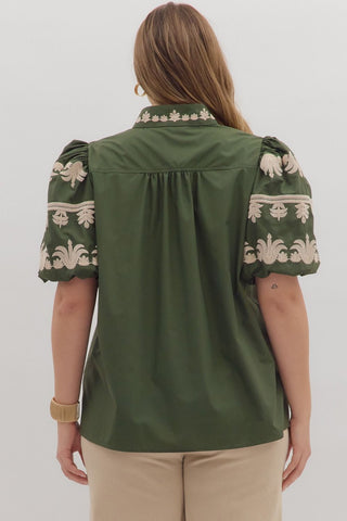 Green blouse with floral embroidery on sleeves and collar worn by a person on a white background