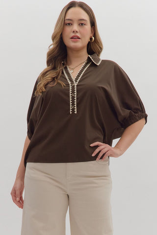 Woman wearing a brown blouse with decorative trim on a white background