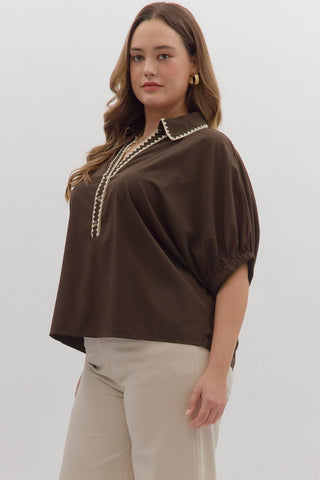 Woman wearing a brown blouse with pearl details and beige pants on a white background