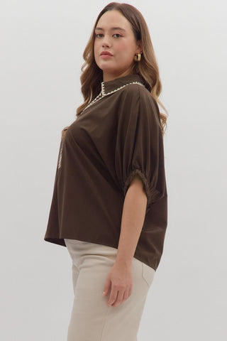 Woman wearing a brown blouse with a pearl necklace against a white background