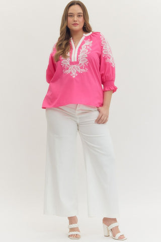 Woman wearing a pink embroidered blouse and white pants on a white background