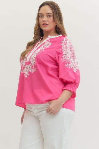 Woman wearing a pink blouse with white embroidery on a plain background